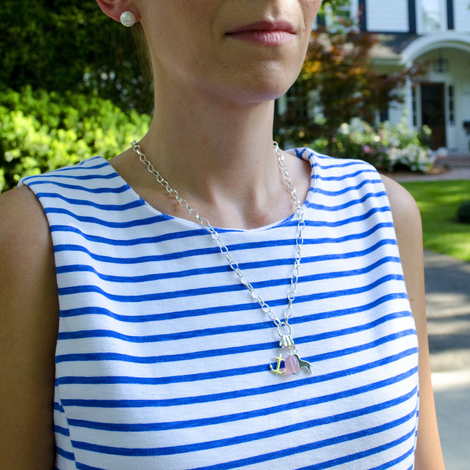 Woman wearing sterling silver charm necklace with sterling silver anchor charm, light pink chalcedony charm and sterling silver dog charm