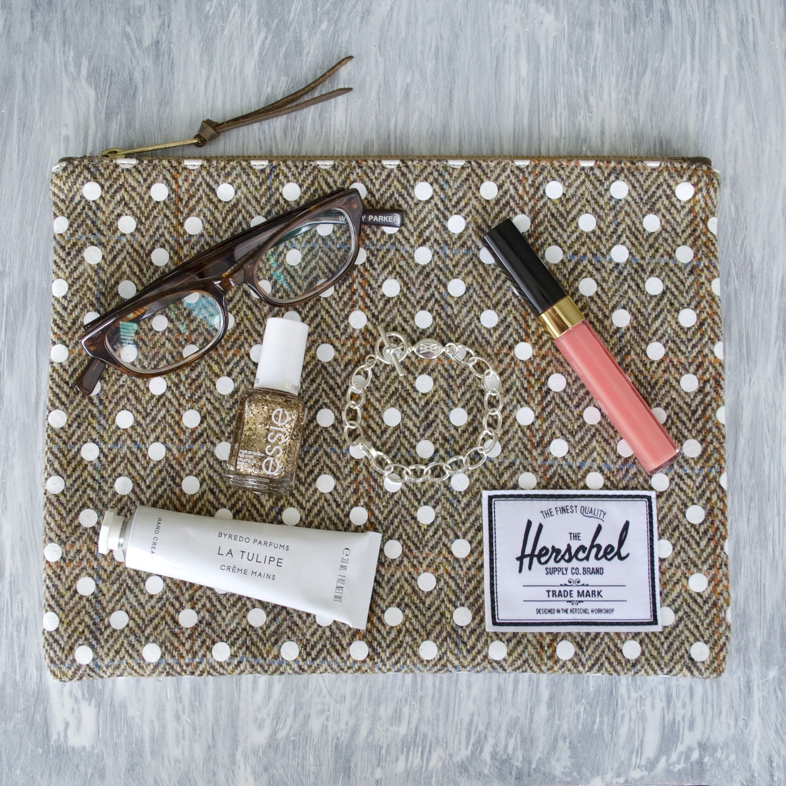 Herschel Pouch with Essie Glitter Nail Polish, Warby Parker glasses, sterling silver charm bracelet, Chanel lip gloss, Byredo La Tulipe hand lotion